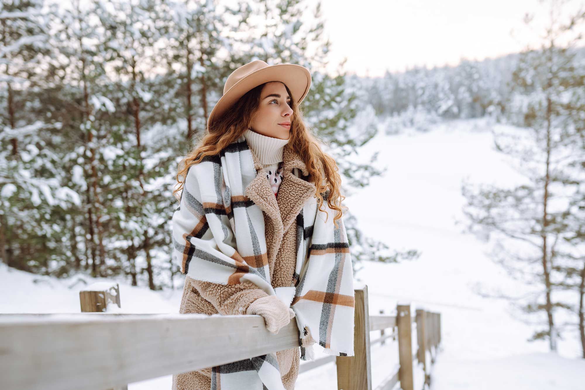 Stylish woman leaning against a wood railing in a snowy forest landscape.jpeg